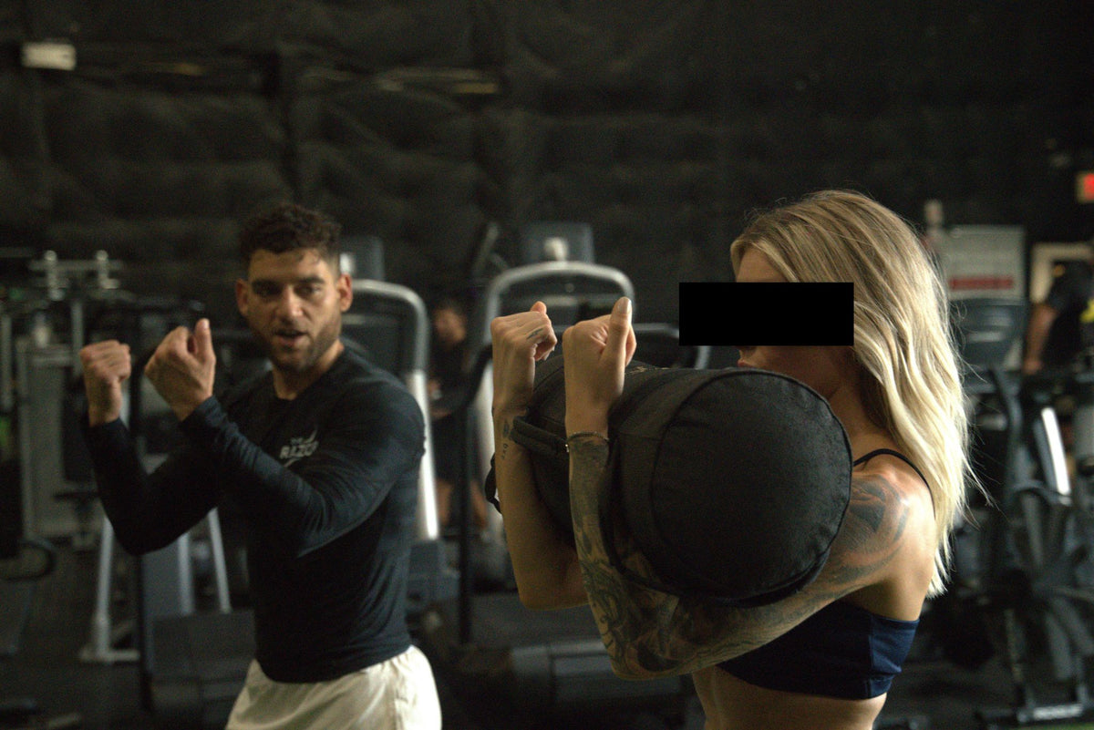 Athlete training with a heavy sandbag while a coach demonstrates